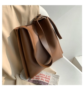 Detail of a large brown leather tote bag leaning against soft beige fabric on white background
