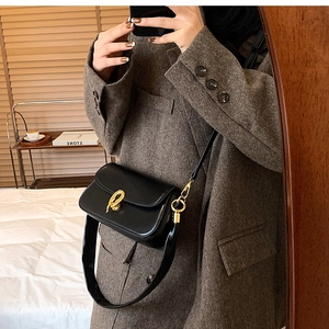 Detailansicht einer schwarzen Ledertasche mit einer goldenen abstrakten Metallschnalle