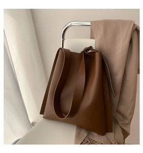 Detail shot of a brown leather tote bag with wide shoulder strap on a designer chair