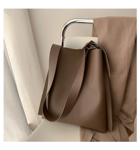 Detail view of coffee brown PU leather tote bag with wide strap on a white chair