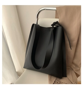 Close-up of a minimalist black leather tote bag with a wide shoulder strap on a white chair