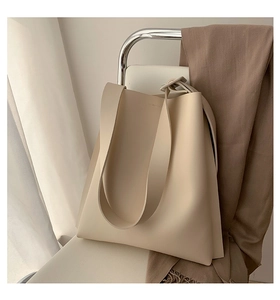 Minimalist cream tote bag in textured faux leather resting on a sleek modern chair