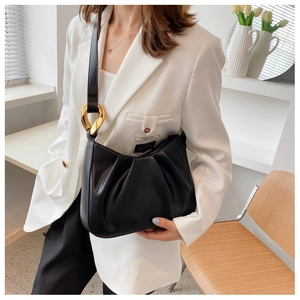 Detailed close-up of a black ruched handbag with shiny gold metal hardware on a white suit