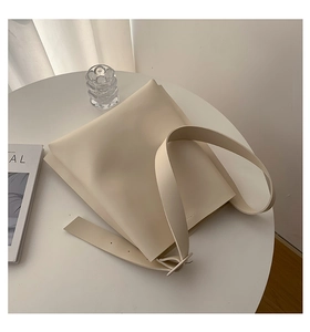 Detailed view of the cream leather tote bag with wide strap on a minimalist background
