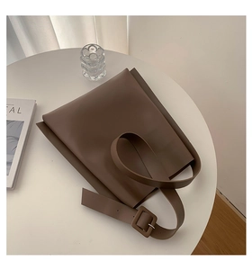Detailed view of brown leather tote bag with wide strap and square buckle on a minimalist table