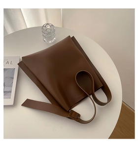 Close-up of a dark brown large tote bag in matte leather on a white table