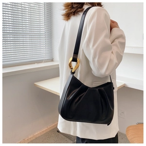 Close-up of black pleated leather shoulder bag featuring a chunky gold metal ring detail