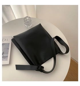Detail view of large black minimalist shoulder bag with wide strap on a modern white table