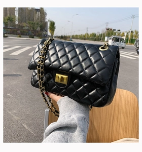 Close-up of black quilted crossbody bag with gold chain strap held by a model outdoors