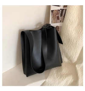 Close-up of black tote bag with wide strap and buckle detail on minimalist background
