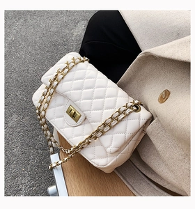 Detail of cream quilted crossbody bag with gold chain strap on a wooden bench