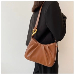 Close-up of brown pleated shoulder bag featuring a modern gold metal knot detail on strap