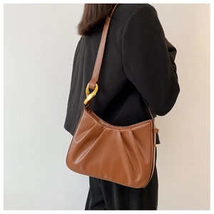 Detail of brown pleated cloud bucket bag with gold metal buckle on model shoulder