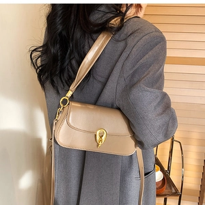 Schicke beige Schultertasche mit goldenem Drehverschluss, getragen von einem Model