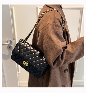 Close-up of black quilted leather bag with gold clasp and interwoven chain strap on shoulder