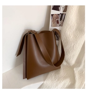 Detail of a large brown leather tote bag with wide shoulder strap on a minimalist background