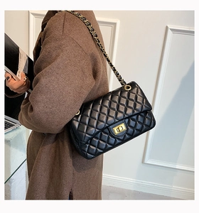 Model wearing black quilted leather crossbody bag with gold chain strap and metal clasp