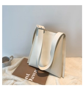 Detail of minimalist cream leather tote bag featuring wide shoulder strap and square buckle