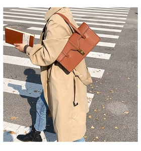 Brown rectangular shoulder bag styled with a beige trench coat in an urban street setting