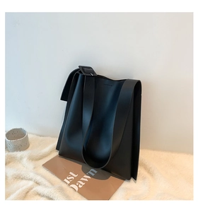 Detail of minimalist black tote bag with wide shoulder strap and square buckle on rug