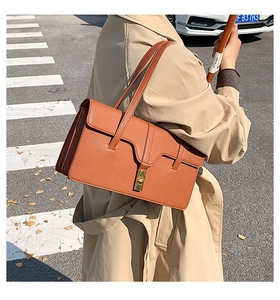 Close-up of a vintage brown leather shoulder bag with a gold buckle on a stylish model