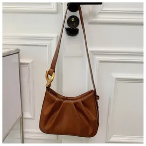 Detail view of brown pleated cloud bag with gold chain strap on an ivory door handle
