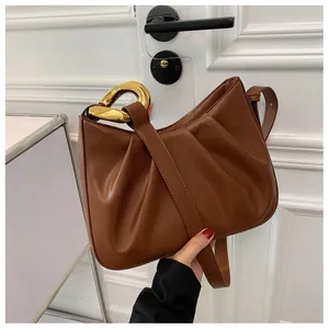 Detail of pleated brown leather bucket bag with polished gold metal handle and strap