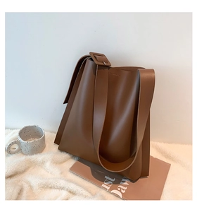 Detail of dark brown tote bag with wide shoulder strap resting on soft white fabric