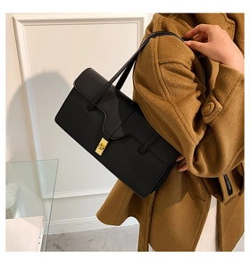 Detail of black leather shoulder bag with gold rectangular clasp and cross-strap design