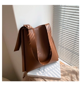 Brown leather tote bag with wide strap reflecting sunlight through blinds for a chic look