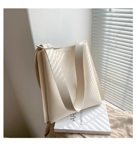 Close-up of minimalist cream leather tote bag with wide strap on a decorative prop