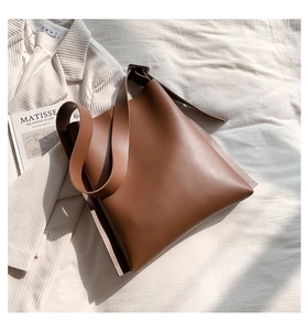 Close-up of minimalist brown leather tote bag with wide strap on aesthetic bedding