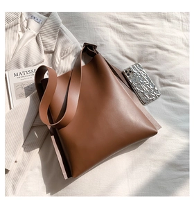 Close-up of caramel brown leather tote bag on white linen with stylish lifestyle props