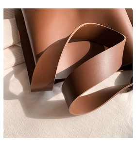 Close-up of premium brown leather texture and wide shoulder strap on a tote bag