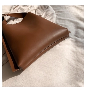Detail view of premium brown leather tote bag with wide shoulder straps on knit surface