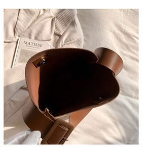Detail view of brown leather bucket bag with magnetic closure and wide shoulder strap