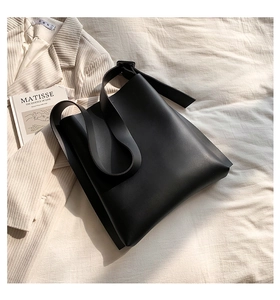 Macro shot of minimalist black matte leather tote bag on beige blazer and art book