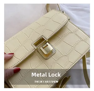Detailed close-up of cream crocodile pattern leather bag with golden hardware lock
