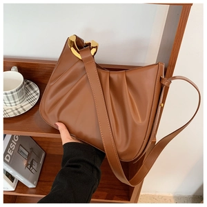 Close-up of brown pleated cloud bucket bag with gold metal rings and leather strap