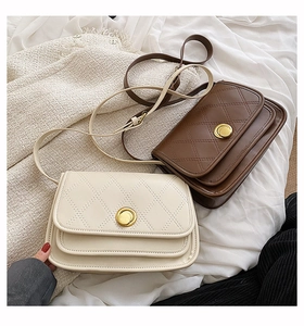 Detail of quilted leather crossbody bags with gold rotary buckles on a textured surface
