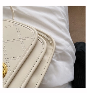 Detail of cream quilted shoulder bag showing fine stitching and gold metal lock