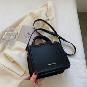 Fashionable black leather crossbody biscuit bag with gold letters on a white blazer