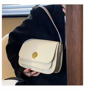 Detail of off-white quilted shoulder bag with golden round rotary buckle on black blazer