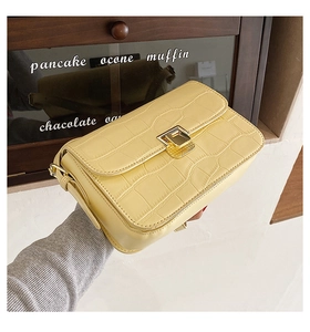 Detailed close-up of cream yellow faux crocodile skin texture and gold buckle on handbag