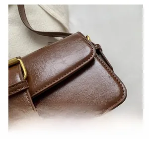 Close-up of retro brown leather handbag showing gold buckle and neat white stitching detail