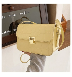 Close-up of pale yellow crossbody bag with crocodile pattern and golden metal lock