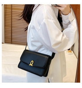 Detail of a black leather rectangular flap bag featuring a stylish gold ring metal buckle