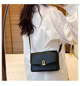 Structured black leather crossbody bag with artistic gold clasp shown on shoulder