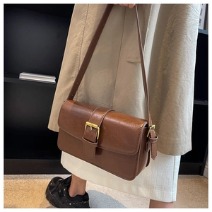 Close-up of vintage brown leather shoulder bag with golden buckle on a beige coat
