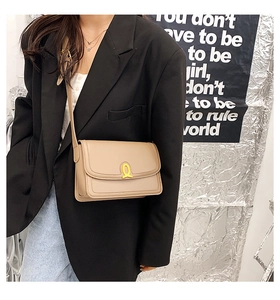 Chic beige leather shoulder bag with a gold ring buckle shown on a model in a fashion setting